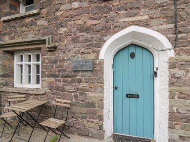 A stone wall with a blue arched door and wooden chairs and table outside at Clifford Place