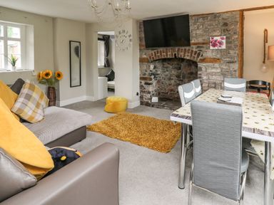 A living room with a sofa pillows a dining table chairs a wall clock and a television above a stone fireplace at Yewtree Cottage in Defynog near Sennybridge