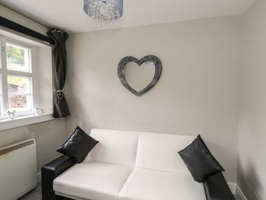 A room with a white and black sofa with black cushions a heart shaped mirror on the wall and a window with curtains at Yewtree Cottage in Defynog near Sennybridge