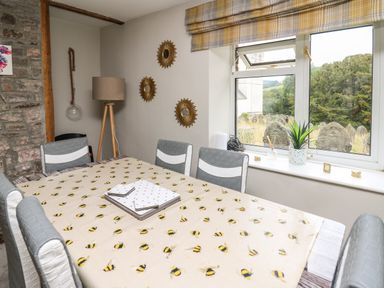 A dining room with a bee patterned tablecloth and grey chairs near a window showing gravestones at Yewtree Cottage in Defynog near Sennybridge