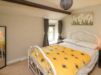 A bedroom with a bed covered with a yellow blanket with bees and a white metal headboard at Yewtree Cottage in Defynog near Sennybridge