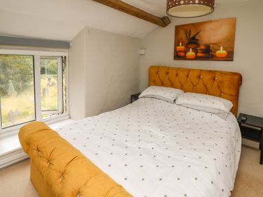 A bedroom with a bed with an orange headboard and footboard next to a window at Yewtree Cottage in Defynog near Sennybridge