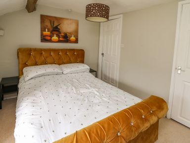 A bedroom with a bed with a mustard velvet headboard and footboard with white bedding and two white doors in Yewtree Cottage Defynog near Sennybridge
