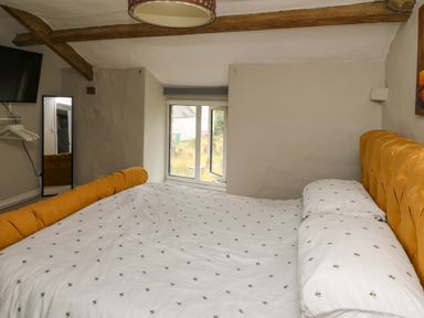 A bedroom with a bed with white sheets and yellow headboard a window a wall mirror and a wall mounted television at Yewtree Cottage in Defynog near Sennybridge