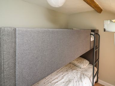 A bunk bed with grey upholstered frame and white bedding with pillow in a room at Yewtree Cottage in Defynog near Sennybridge