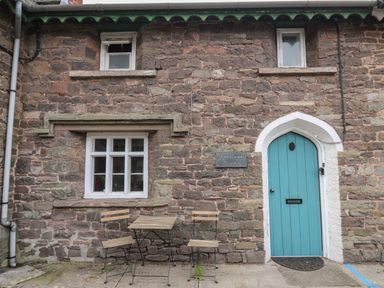 A stone building with a blue arched door two windows and a small table with two chairs outside Clifford Place