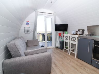 A compact living area with a gray sofa TV kitchen appliances and two bar stools at Owl's Nook Kilkhampton