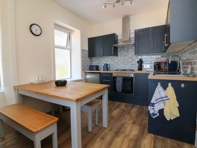 A kitchen with wooden table and benches navy cabinets stove and microwave at At the Bay Apartment in Hele Bay Ilfracombe