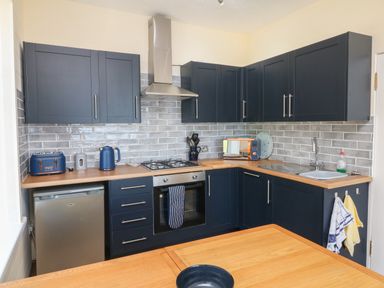 A kitchen with dark blue cabinets a stainless steel oven and fridge a wooden countertop and grey tiled backsplash at At the Bay Apartment in Hele Bay Ilfracombe