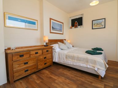 A bedroom with a wooden bed and dresser with lamps and framed pictures on the walls at At the Bay Apartment in Hele Bay Ilfracombe