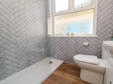 A bathroom with a glass shower, a toilet, wood flooring, and a frosted window at At the Bay Apartment in Hele Bay Ilfracombe
