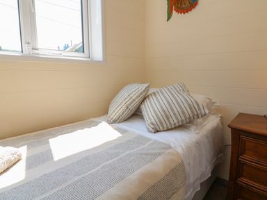 A bedroom with a bed with two pillows and a striped blanket next to a wooden nightstand at At the Bay Apartment Hele Bay Ilfracombe