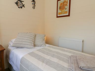A bedroom with a single bed striped bedding pillows a wooden nightstand wall decorations and a framed sunflower painting at At the Bay Apartment in Hele Bay Ilfracombe