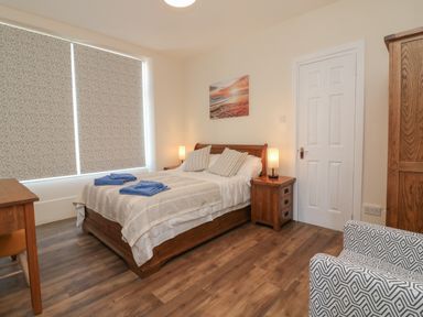 A bedroom with a bed with two blue towels bedside tables lamps a patterned chair and wooden furniture at At the Bay Apartment in Hele Bay Ilfracombe