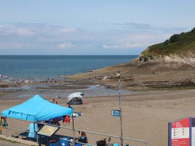 A beach with people swimming and tents near a rocky shoreline at At the Bay Apartment in Hele Bay Ilfracombe