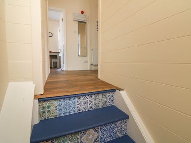 A small set of stairs with patterned tiles leading to a hallway with wooden flooring and a wall mirror at At the Bay Apartment in Hele Bay Ilfracombe