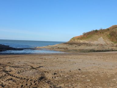A sandy beach with tire tracks and rocky cliffs by the sea at At the Bay Apartment in Hele Bay Ilfracombe