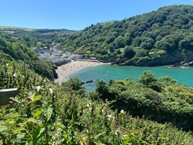 A coastal bay with a sandy beach people on the beach and in the water surrounded by green hills at At the Bay Apartment in Hele Bay Ilfracombe