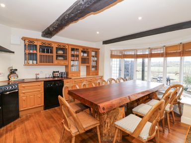 A kitchen with wooden cabinets and a large wooden dining table with chairs by a bay window at Riverside Manor in Evesham