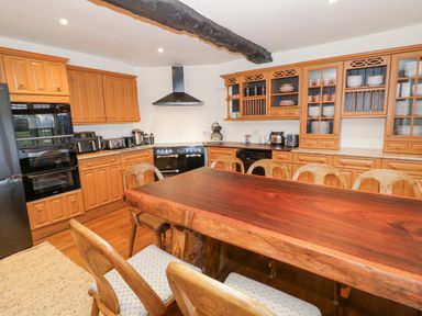 A kitchen with wooden cabinets a wooden dining table with chairs black appliances and a black ceiling beam at Riverside Manor in Evesham