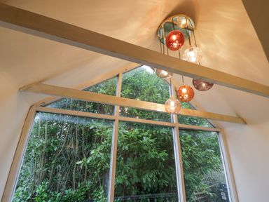 A large triangular window with beams and hanging round light fixtures showing trees outside at Riverside Manor in Evesham