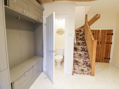 A hallway with a built-in grey cabinet open door showing a toilet next to stairs with floral carpet and wooden gate at Riverside Manor in Evesham