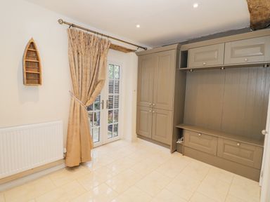 A room with beige tiled floor a grey built in cabinet beige curtains on glass door and a wooden boat shelf on the wall at Riverside Manor in Evesham