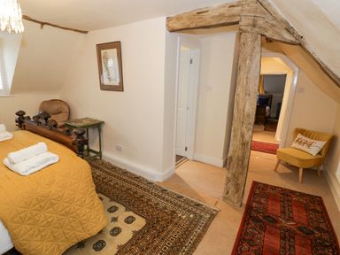 A bedroom with a wooden bed with a yellow quilt and towels a wooden beam a yellow chair with a pillow and patterned rugs at Riverside Manor in Evesham