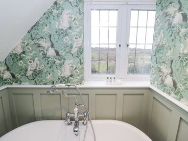 A bathtub with metal taps under a window with landscape view and floral bird wallpaper at Riverside Manor in Evesham