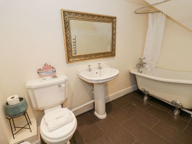 A bathroom with a toilet, pedestal sink, ornate mirror, clawfoot bathtub with shower curtain at Riverside Manor in Evesham
