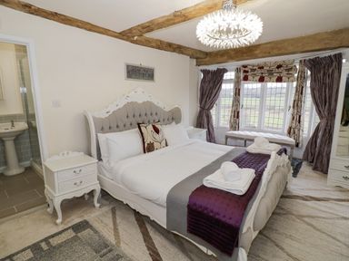 A bedroom with a bed folded towels bedside tables a bench in front of a window and bathroom visible at Riverside Manor in Evesham