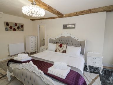 A bedroom with a large ornate bed white furniture wooden ceiling beams and a floral painting at Riverside Manor in Evesham