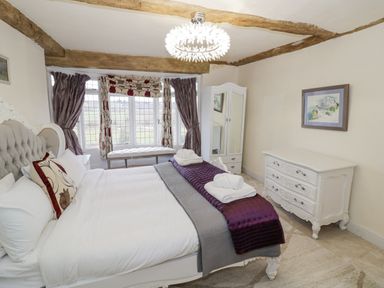 A bedroom with a bed and pillows near a window with curtains and a bench with a wardrobe and dresser on the side at Riverside Manor in Evesham