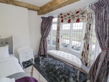 A bedroom with a bed side table a window with curtains and a bench on a rug at Riverside Manor in Evesham