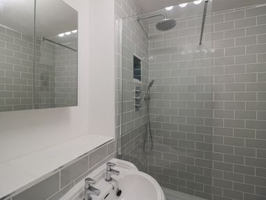 A bathroom with a white sink, dual taps, a mirrored cabinet, and a walk-in shower with grey tiled walls at Riverside Manor in Evesham