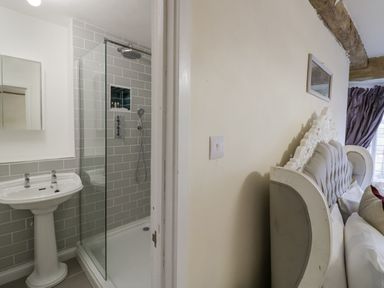 A bathroom with a pedestal sink and glass shower next to a bedroom with a bed and decorative headboard at Riverside Manor in Evesham