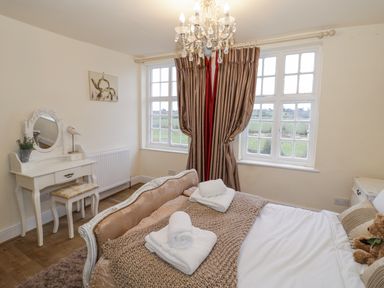 A bedroom with a bed a dressing table and windows with curtains at Riverside Manor in Evesham