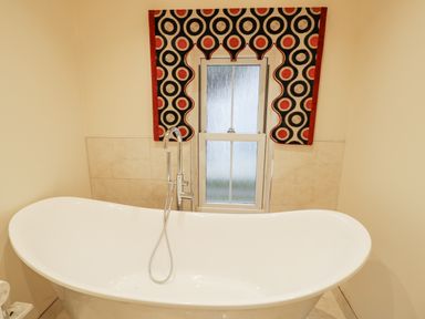 A bathroom with a white freestanding bathtub under a window with a patterned valance at Riverside Manor in Evesham
