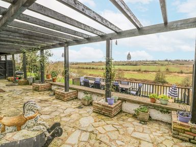 A covered stone patio with potted plants and outdoor dining furniture overlooking a grassy field at Riverside Manor in Evesham