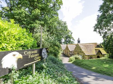 A sign for Cotswold Falconry Centre beside a tree-lined path leading to stone buildings at Riverside Manor in Evesham