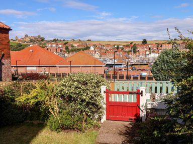 A garden with bushes and a red gate overlooking buildings and a harbor at Whitby View in Whitby