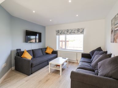 A living room with two gray sofas, a white coffee table, a wall-mounted TV, and a window with a patterned blind at Whitby View in Whitby