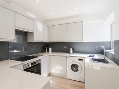 A kitchen with white cabinets a washing machine an oven stovetop a kettle and a sink at Whitby View in Whitby