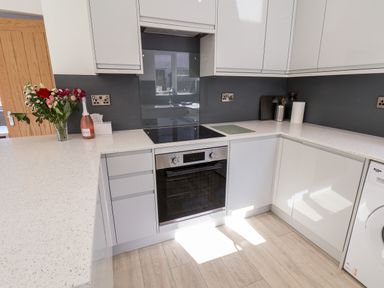 A kitchen with white cabinets a built in oven an electric stove a washing machine and flowers on the counter at Whitby View in Whitby