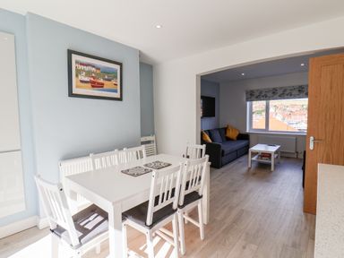 A dining area with a white table and six chairs adjacent to a living room with a sofa and coffee table at Whitby View in Whitby