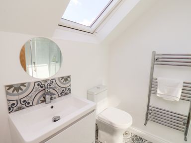 A bathroom with a sink a round mirror a toilet and a heated towel rail at Whitby View in Whitby