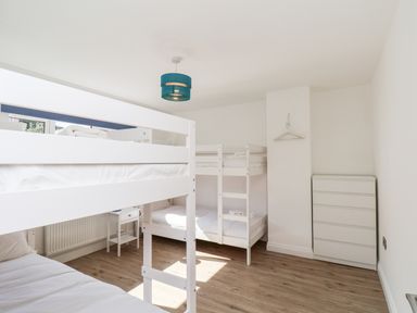 A bedroom with two white bunk beds a small bedside table a white chest of drawers and a blue ceiling light at Whitby View in Whitby
