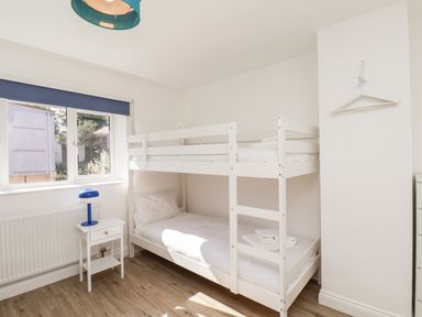 A bedroom with white bunk beds a window with blue blind a small white bedside table and a blue lamp at Whitby View in Whitby