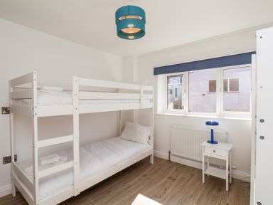 A bedroom with white bunk beds a small white bedside table with a blue lamp and windows at Whitby View in Whitby