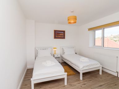A bedroom with two single beds a nightstand with a lamp a small rug and a window showing rooftops at Whitby View in Whitby